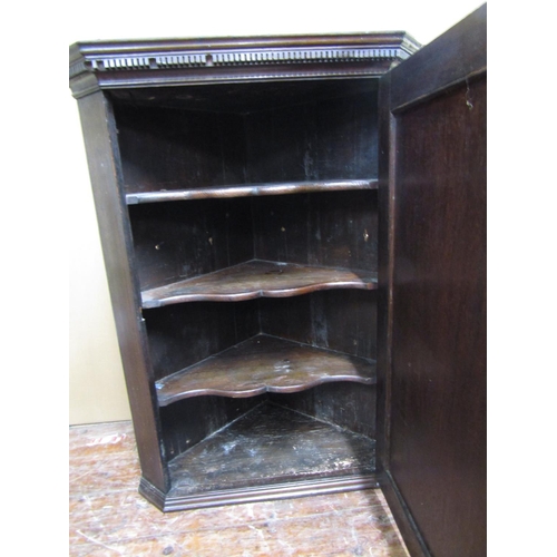 1554 - A Georgian oak hanging corner cupboard enclosed by a single panelled door with shell detail, beneath... 