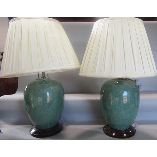 819 - A pair of green crackle glazed table lamps on wooden stands and with silk pleated shades, 66cm high.