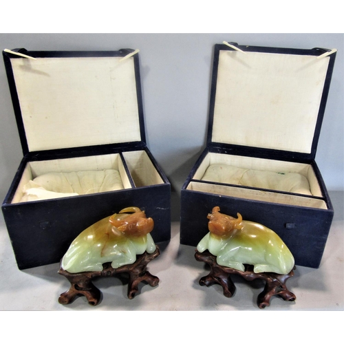 821 - A pair of celadon and russet jade recumbent water buffaloes on carved wooden stands, in original box... 