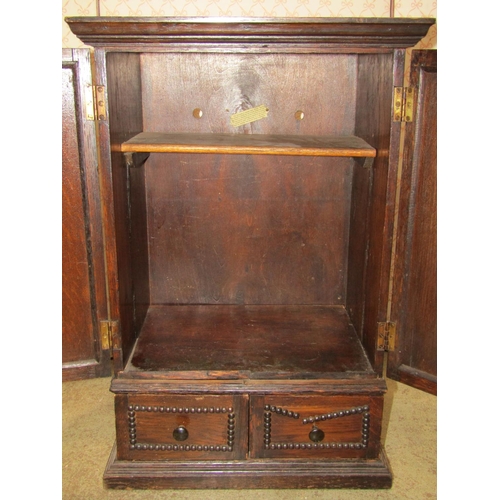 1392 - A small 1920s Jacobean revival oak wall cabinet in the form of a wardrobe enclosed by a pair of thre... 