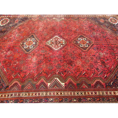 1810 - A large Middle Eastern carpet with three central medallions on a field of stylised flowers on a pred... 