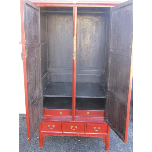 2565 - A red lacquer Chinese wardrobe of tapering form with two panel doors over three drawers, 96cm wide m... 