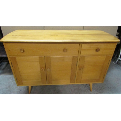 2398 - An Ercol light elm and beechwood dresser base, enclosed by three doors and two drawers, raised on sp... 