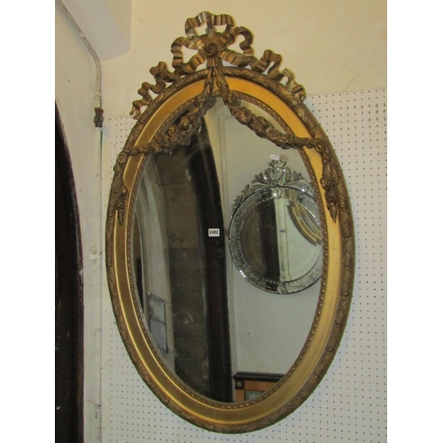 2482 - An antique oval gilt framed wall mirror with tied ribbon surmount 118 cm x 75 cm