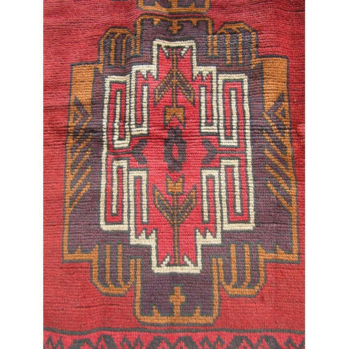 2513 - A Baluchi rug with two central motifs and continuous hook border in deep tones of crimson, wine, sie... 