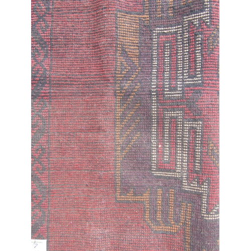 2513 - A Baluchi rug with two central motifs and continuous hook border in deep tones of crimson, wine, sie... 