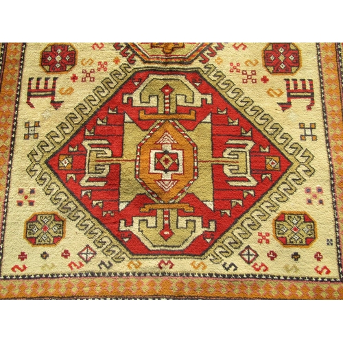 2523 - A Turkish Kazak rug with three central hooked medallions in neutral tones of ochre, vermillion and s... 