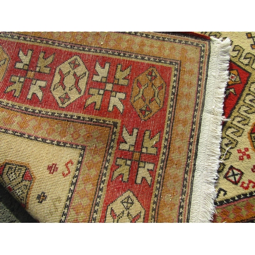 2523 - A Turkish Kazak rug with three central hooked medallions in neutral tones of ochre, vermillion and s... 