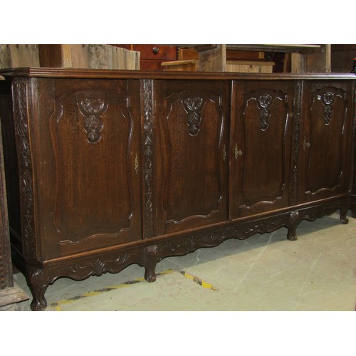 2439 - A substantial continental oak buffet enclosed by four fielded panelled doors with carved shell and f... 