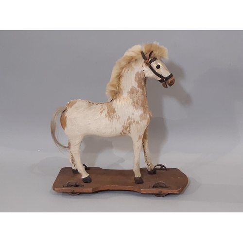 369 - Pull along horse; a small pony skin horse, mounted on a pine base and with metal wheels to each corn... 