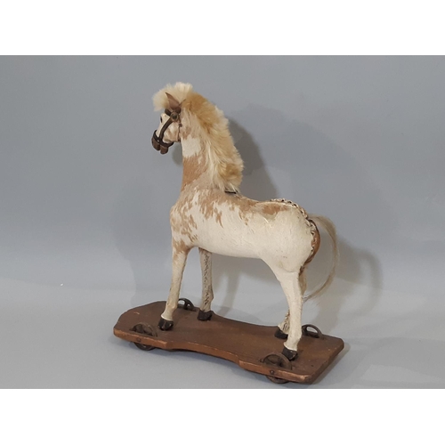 369 - Pull along horse; a small pony skin horse, mounted on a pine base and with metal wheels to each corn... 