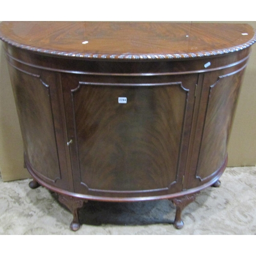 2294 - An Edwardian mahogany demi-lune side cupboard enclosed by a central door with applied mouldings and ... 