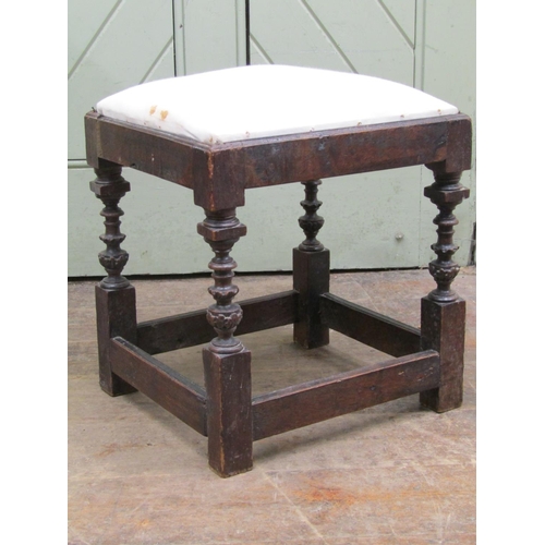 2679 - An antique oak stool with upholstered top raised on four turned and carved supports