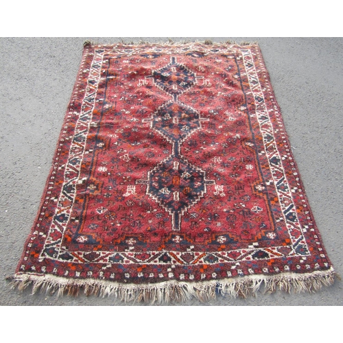 1702 - A Middle Eastern carpet with triple linked lozenge on a red ground, 190cm x 140cm approx.