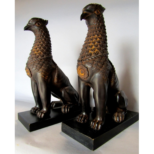 1431 - A pair of wingless Griffins, in a bronze effect finish, raised on slate plinths. 27cm tall