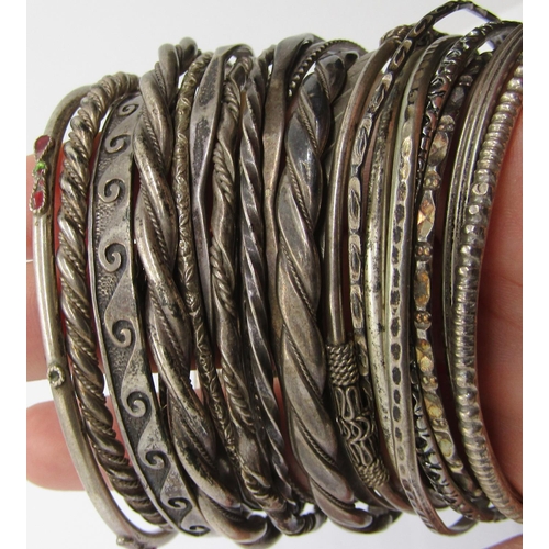 1322 - Twenty-four silver / white metal bangles of various design, to include an enamelled example, wavy de... 