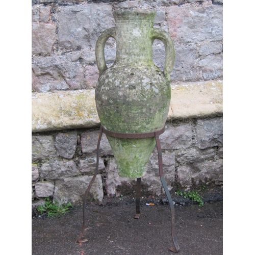 2067 - A weathered clay amphora with moulded loop handles, raised on a simple ironwork stand, 76cm high