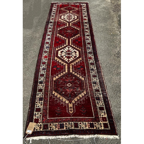 1614 - A Persian runner with a central row interlocking medallions on a red ground, 346cm x 88cm approx.