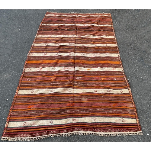 1652 - A North African flat weave carpet in horizontal stripes of ochre, pink and brown interspersed with s... 