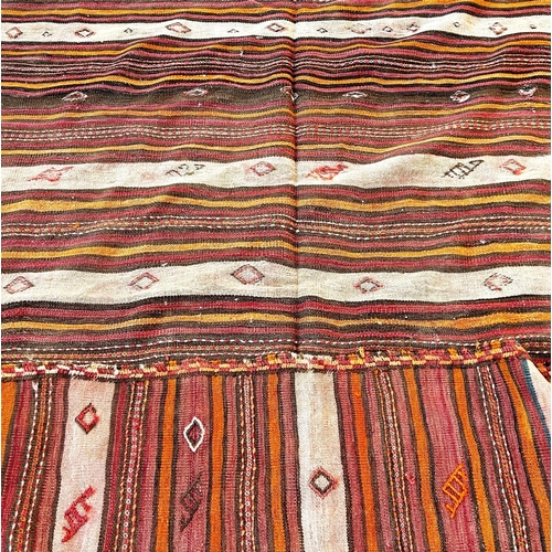 1652 - A North African flat weave carpet in horizontal stripes of ochre, pink and brown interspersed with s... 