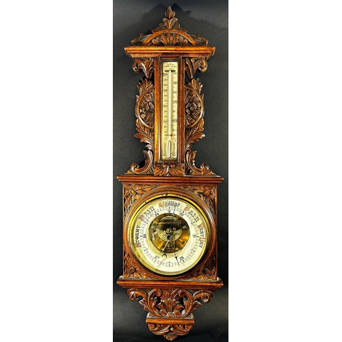 1378 - An Edwardian aneroid barometer in a profusely carved shaped oak case, with enamelled dials