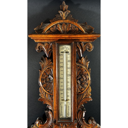 1378 - An Edwardian aneroid barometer in a profusely carved shaped oak case, with enamelled dials