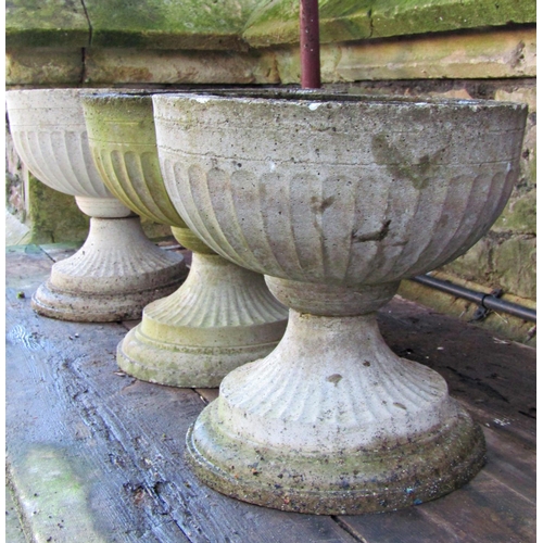 2002 - A set of three weathered cast composition stone squat circular fluted garden urns, with fixed bases,... 