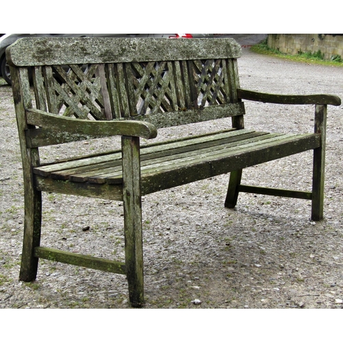 7 - A weathered hardwood three seat garden bench with slatted seat beneath a decorative lattice panelled... 