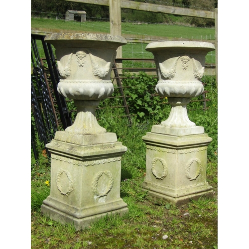 184 - A pair of weathered cast composition stone garden urns with flared rims, repeating face mask and fru... 