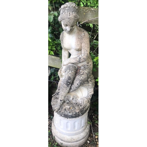 62 - A weathered cast composition stone garden ornament in the form of a seated classical female nude rai... 