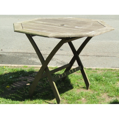 695 - A weathered teak folding garden table with octagonal slatted top 111 cm across