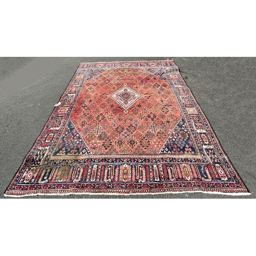 2697 - A Middle Eastern design carpet with a repeating geometric design on a pale red ground, worn in place... 