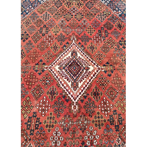 2697 - A Middle Eastern design carpet with a repeating geometric design on a pale red ground, worn in place... 