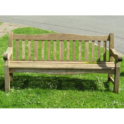 719 - A good quality heavy gauge teak three seat garden bench with slatted seat and back beneath a shaped ... 