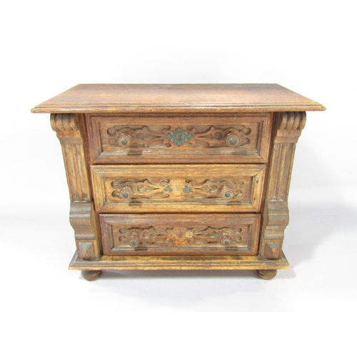 1464 - A miniature oak chest of with three carved panelled drawers, on bun feet, 30cm wide x 24cm high.