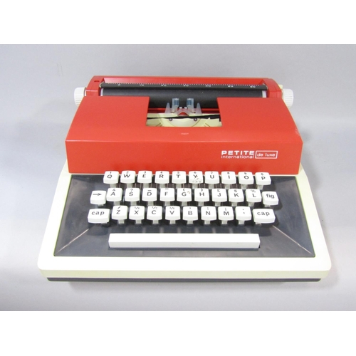 1475 - A 1970’s red and cream plastic Petite International de luxe typewriter, in a hard plastic grey carry... 