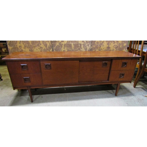 2195 - A long and low mid 20th century teak sideboard partially enclosed by a pair of central sliding doors... 