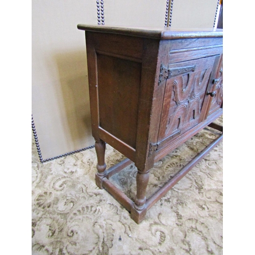 2335 - A rustic carved oak sideboard enclosed by two panelled doors with ironwork hinges on turned supports... 