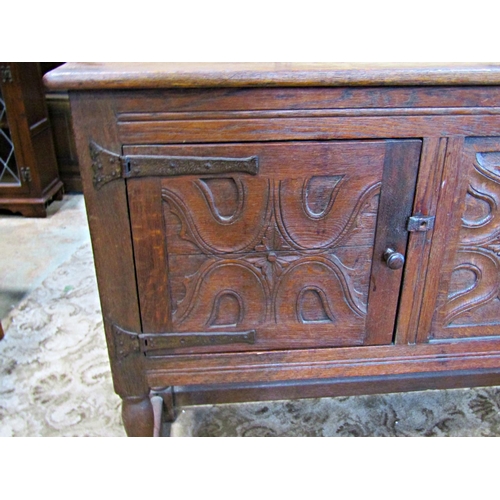 2335 - A rustic carved oak sideboard enclosed by two panelled doors with ironwork hinges on turned supports... 