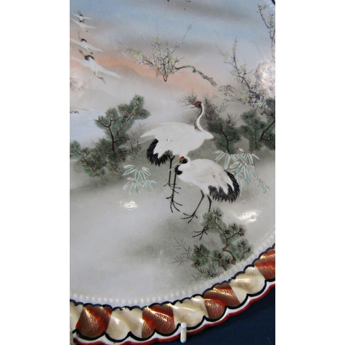 1170C - A Japanese ceramic tray, circular, the central panel cranes, prunus blossom in landscape within a re... 