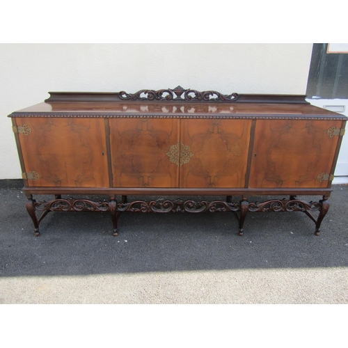A continental walnut veneered sideboard with scrolling pierced carved apron, raised on carved cabriole supports, with pierced brass escutcheon and hinges, united by turned stretchers, 106 cm high x 226 cm x 56 cm