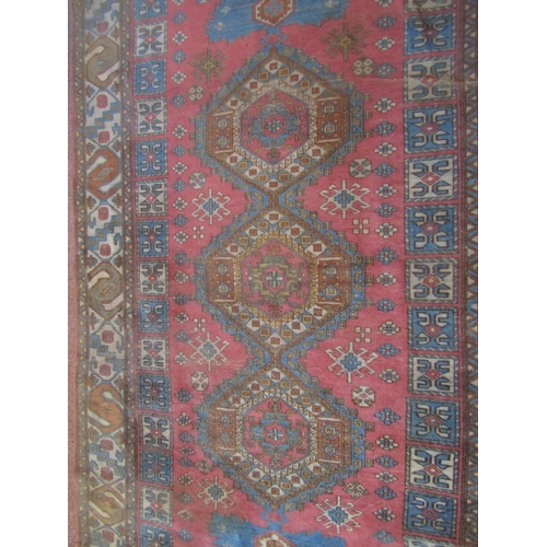 2720 - An eastern wool rug, with triple medallion centre upon a pink field, set within running geometric bo... 