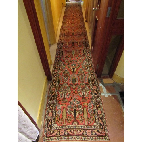 2725 - A very long eastern style runner, with repeating floral and vase detail, upon a pink ground within n... 