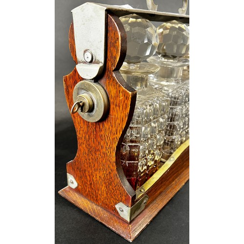 1123 - A late Victorian oak and silver plated three bottle tantalus, with working lock and key, chips to tw... 