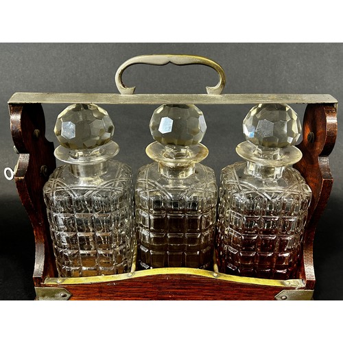 1123 - A late Victorian oak and silver plated three bottle tantalus, with working lock and key, chips to tw... 