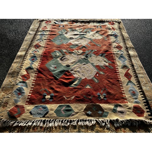 2716 - A large Kilim carpet, with two stylised floral patterns on a pale red ground and repeating geometric... 