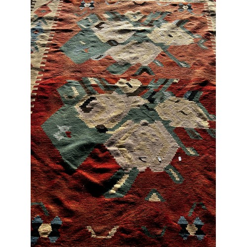 2716 - A large Kilim carpet, with two stylised floral patterns on a pale red ground and repeating geometric... 