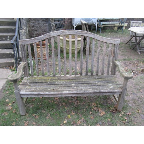 2075 - A weathered teakwood bench with slated seat and back beneath an arched rail, 159cm wide (af)