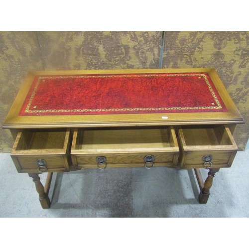 1208 - A reproduction pale oak writing table with inset red leather panelled top over an arrangement of fiv... 