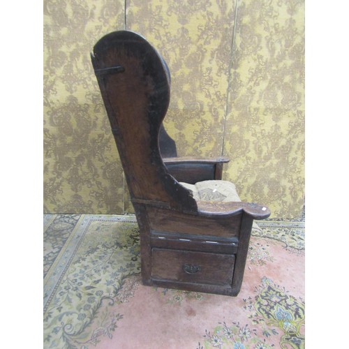 1536 - An 18th century oak lambing chair with fielded panel back and deep winged sides, the shaped arms ove... 